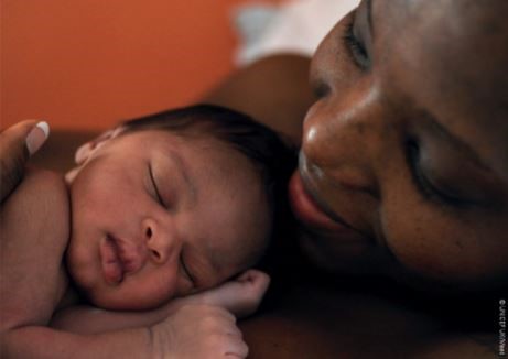 Mother smiles down at sleeping newborn in her arms
