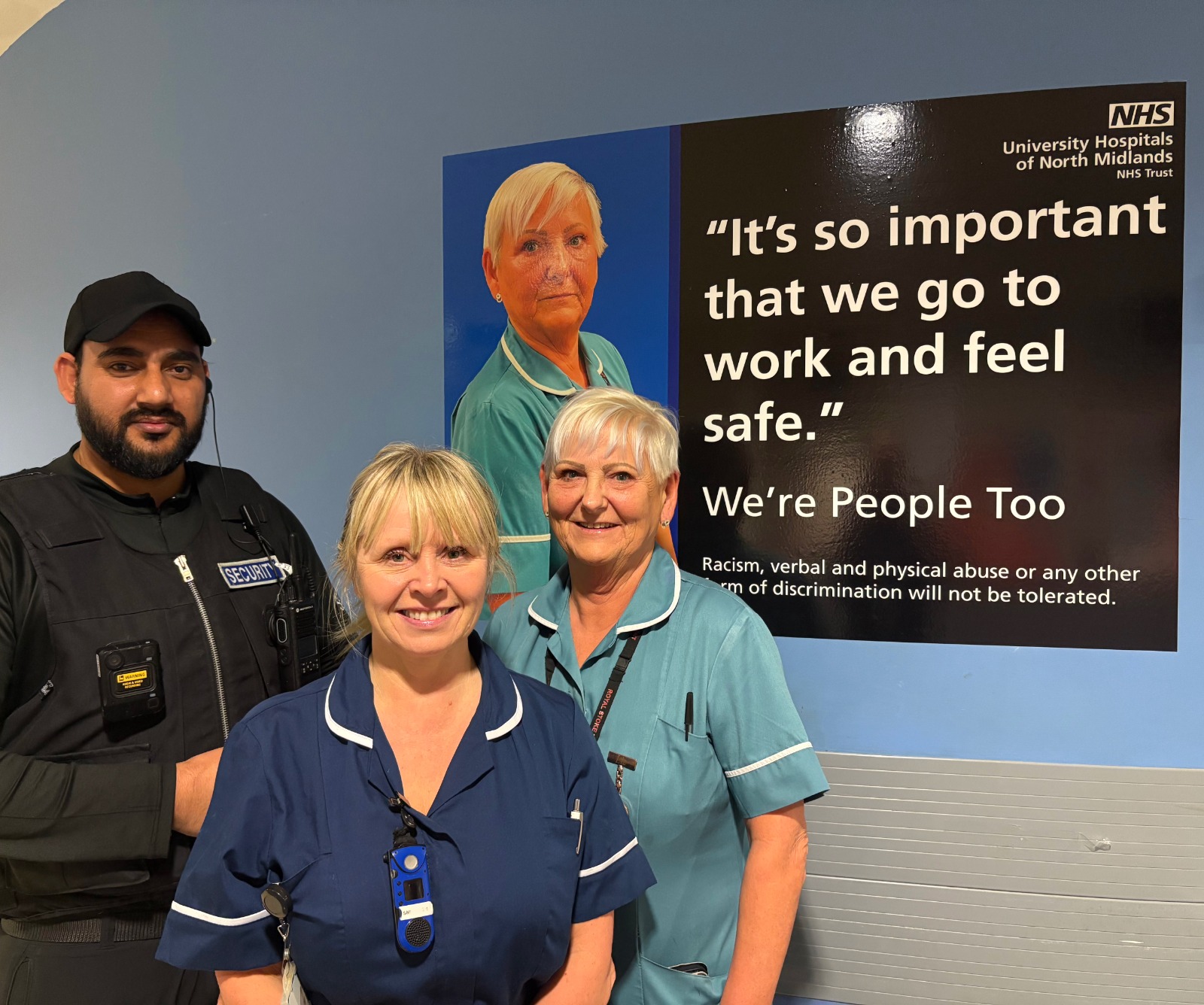 A&E colleagues standing by a large picture for the staff abuse campaign